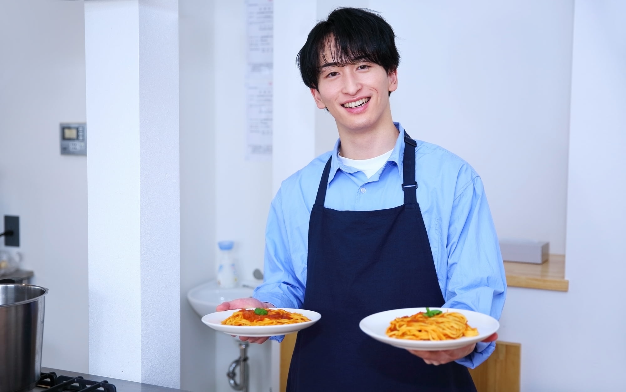 不正咬合を矯正した綺麗な歯並びの男性が料理したパスタを両手に持っている